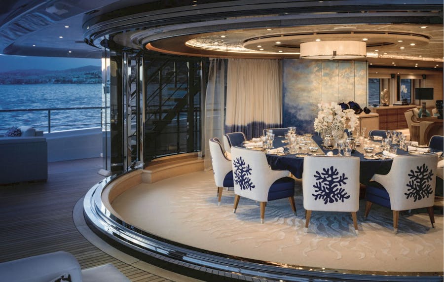 Interior image of the main salong dining area from the aft deck at night. >